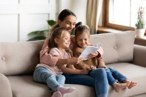 mother and daughters reading a book together on a couch
