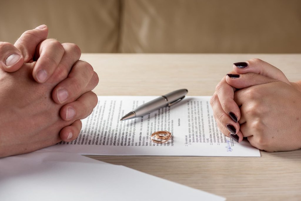man and woman with a divorce contract in between them along with a pen and wedding rings
