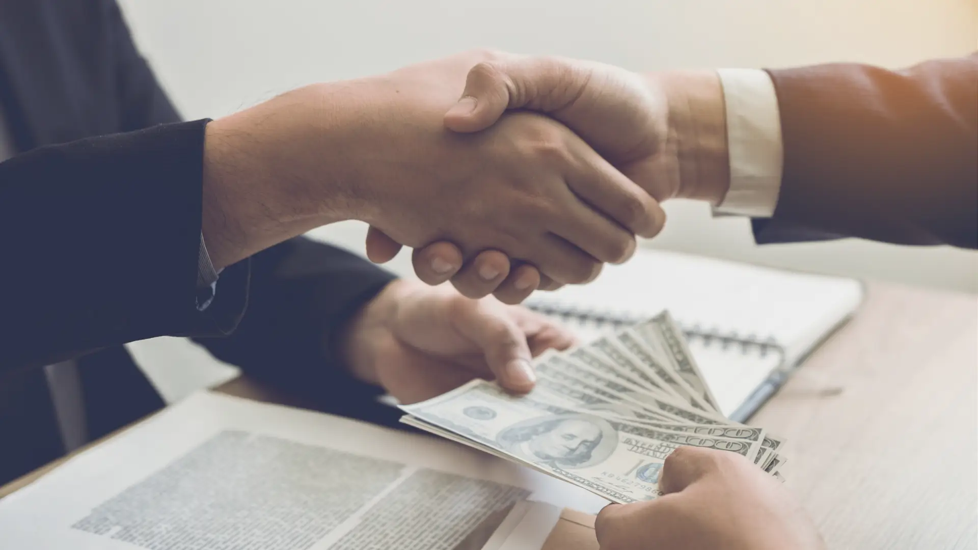 adoption lawyer handing their client USD cash while shaking their hand.
