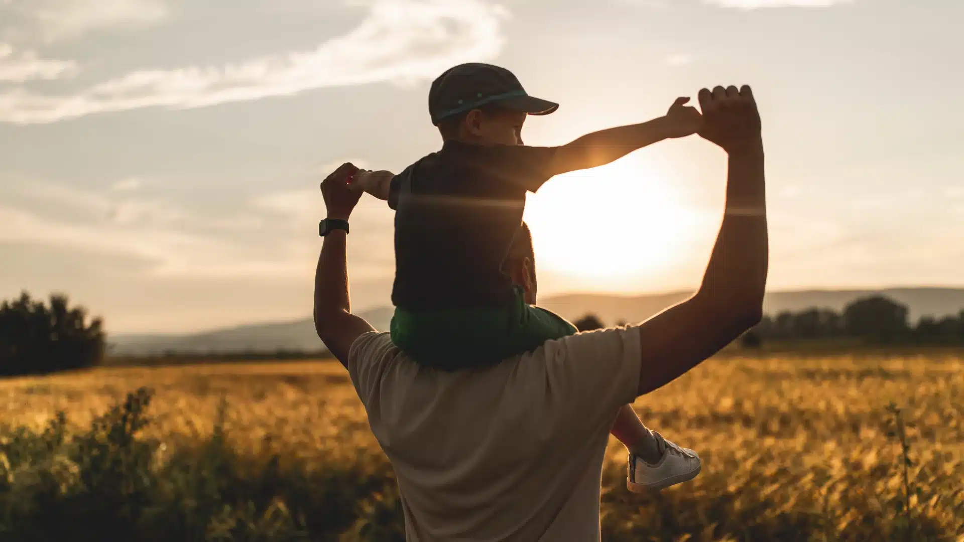 a father carrying their child on their shoulders while holding his hands