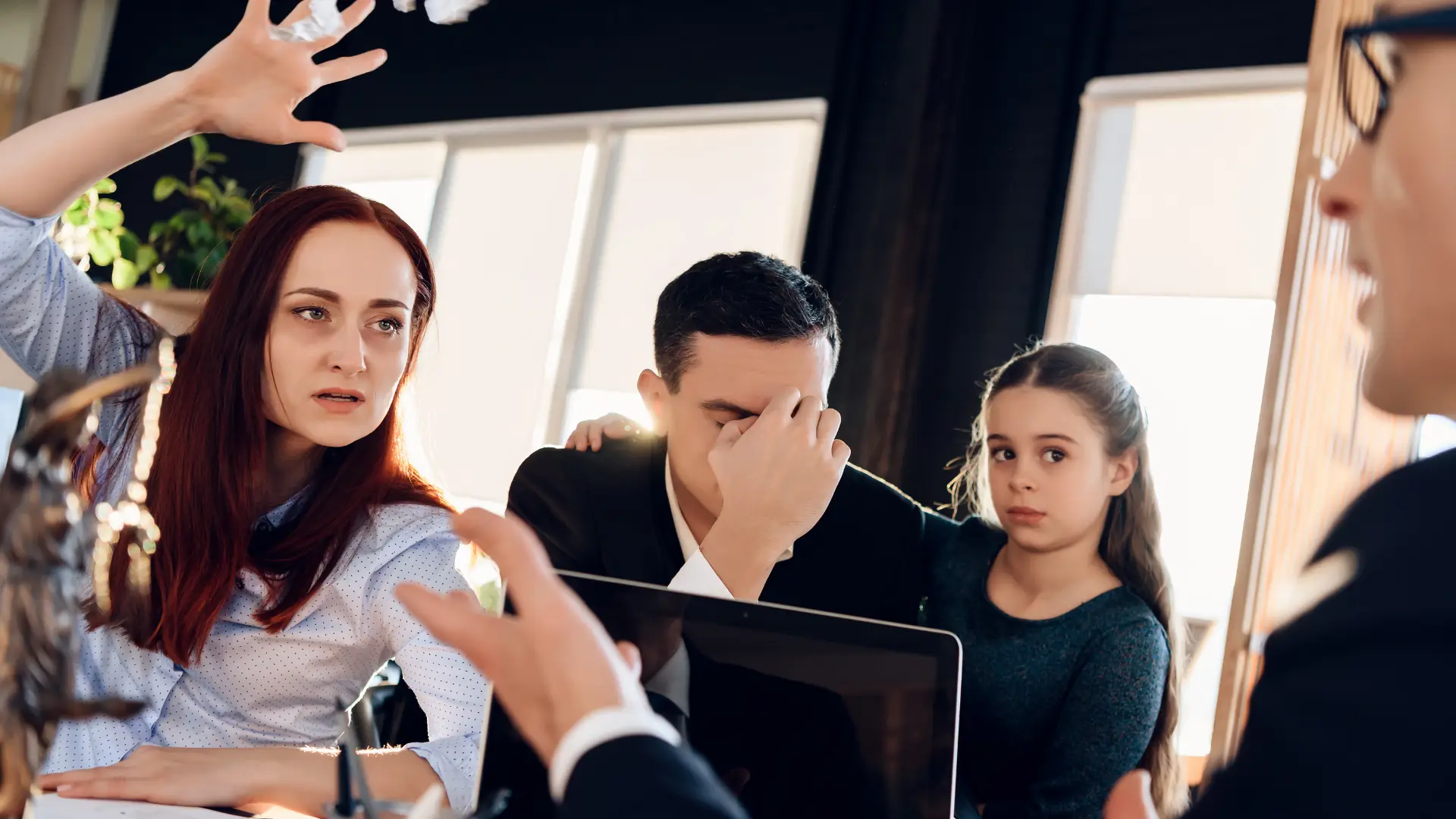 mother raising her hand in a child custody mediation meeting with an upset father and child next to her while family law attorney is listening