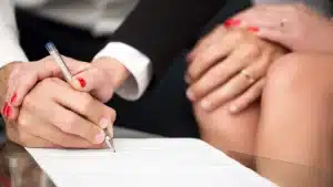 a man signing a document with a hand of a woman on his hand