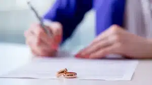 a divorced woman signing a prenup document with 2 wedding bands on top of the document