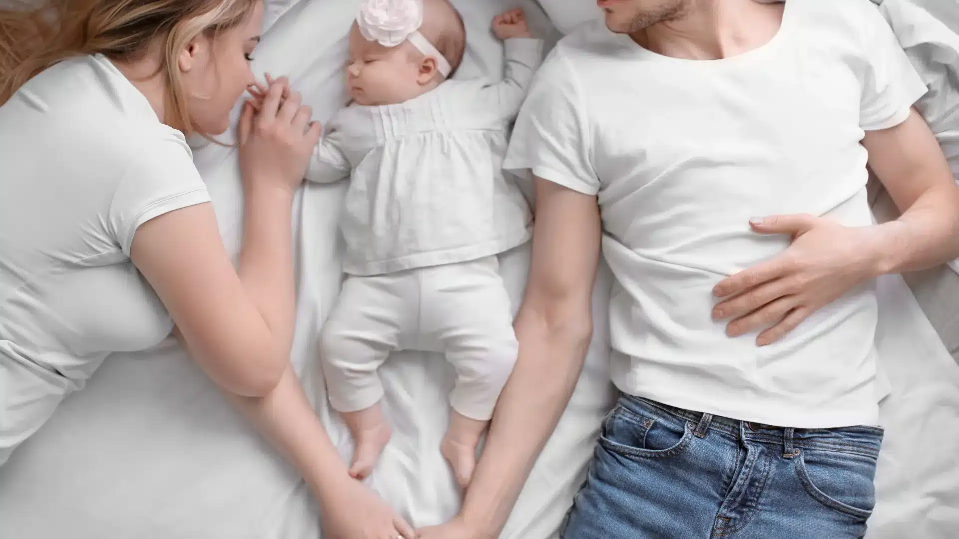 two parents laying down with a baby in between them