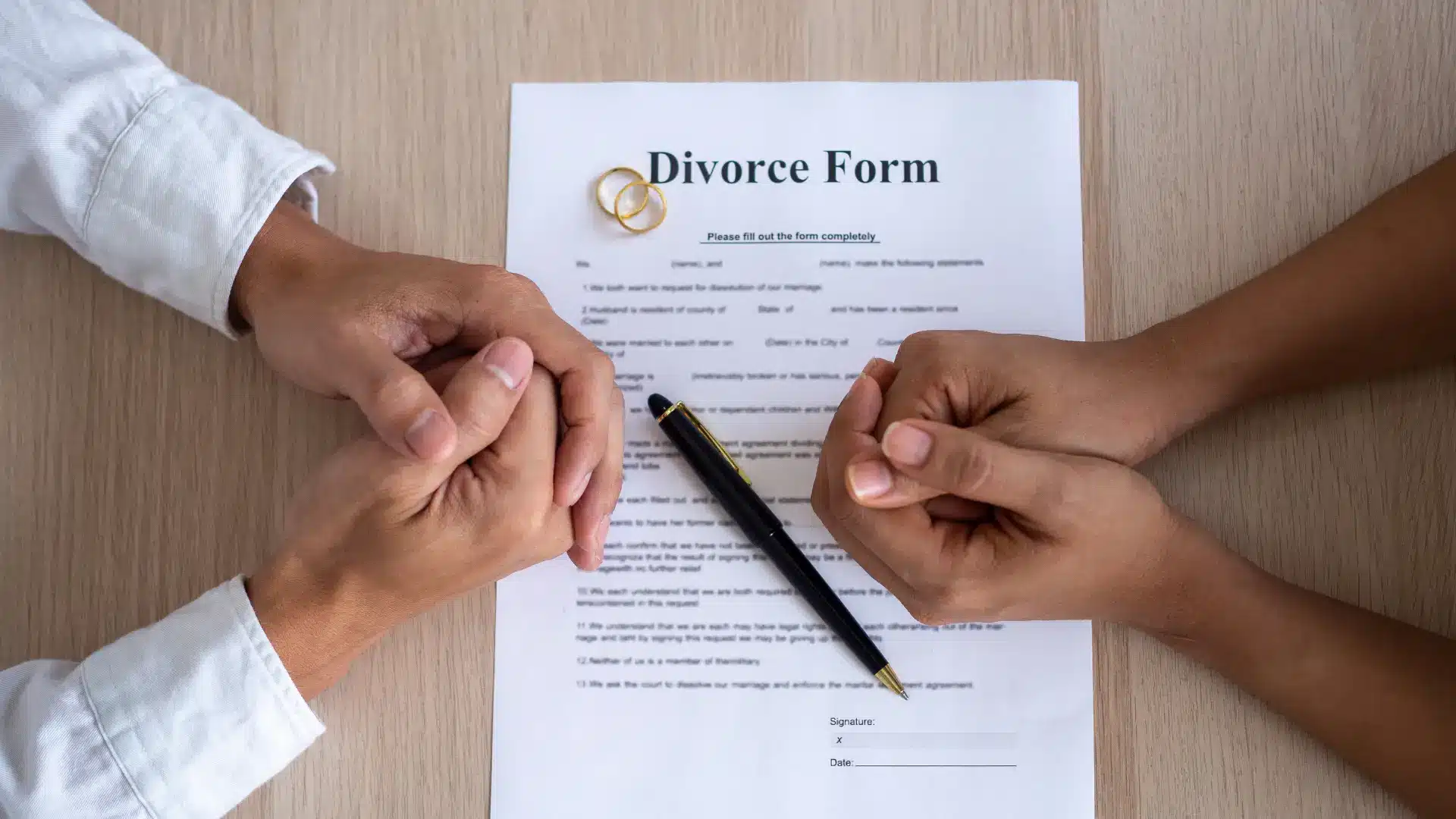 a couple facing their hands with a divorce paper and a pen in between