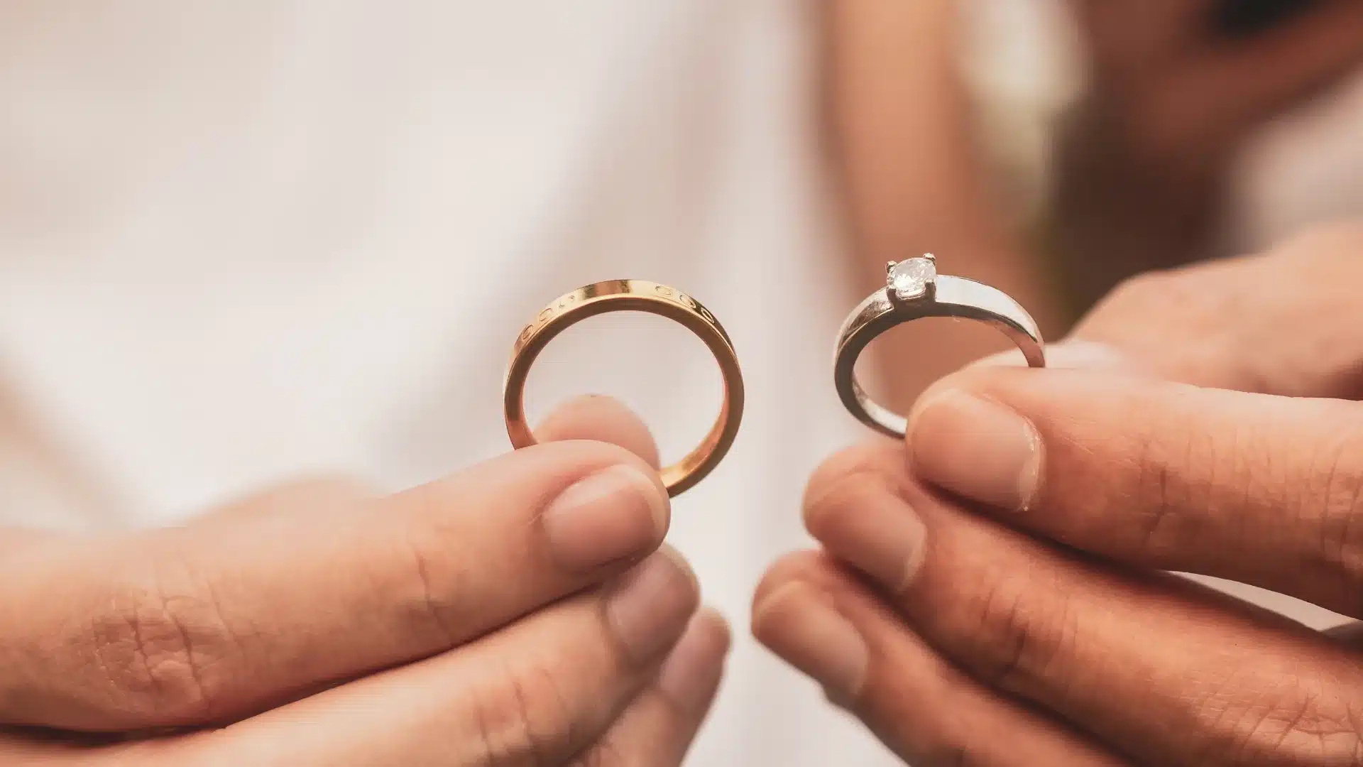 a pair of hands holding a pair of gold rings