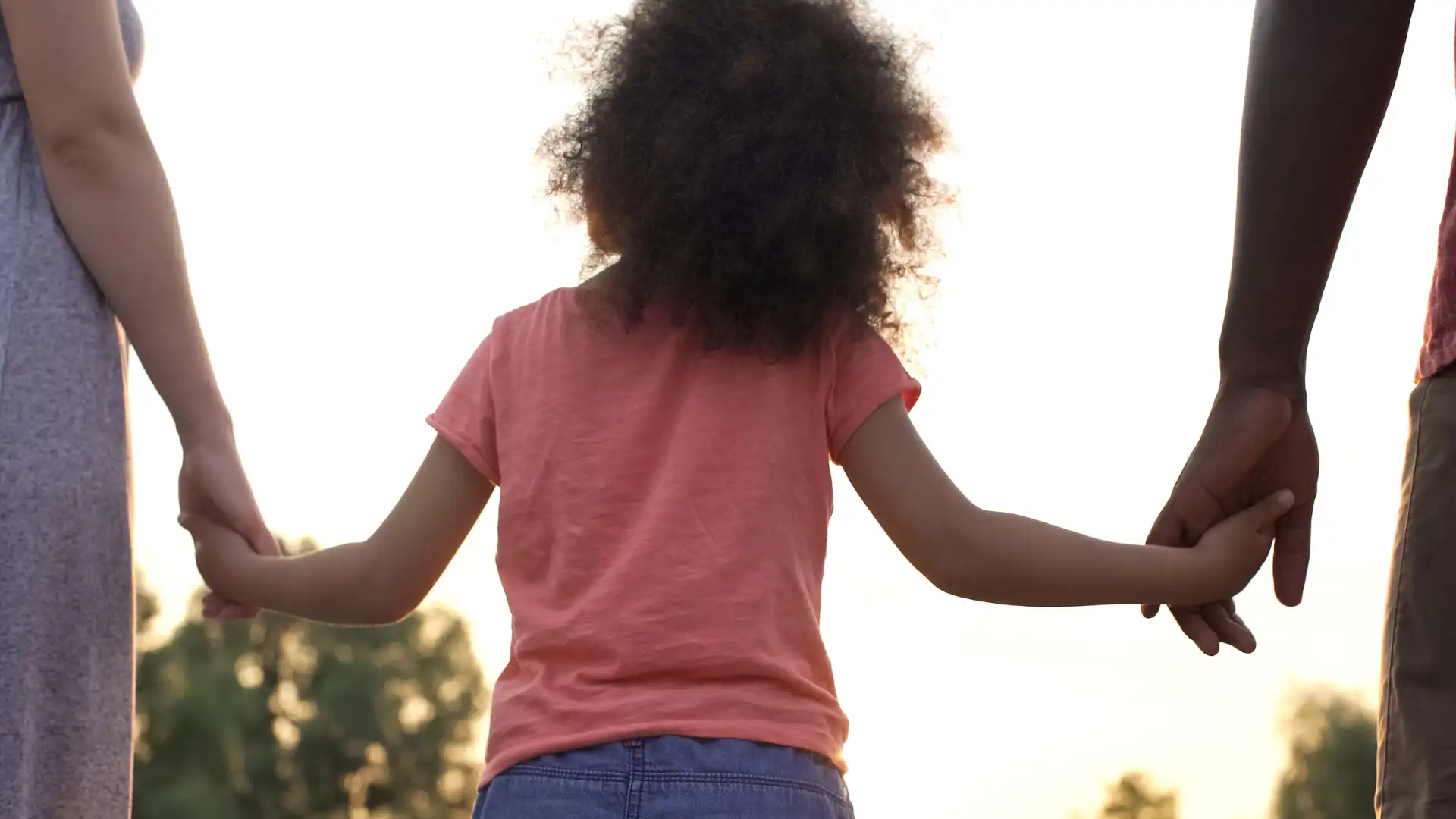 Child with curly hair standing outdoors, arms outstretched
