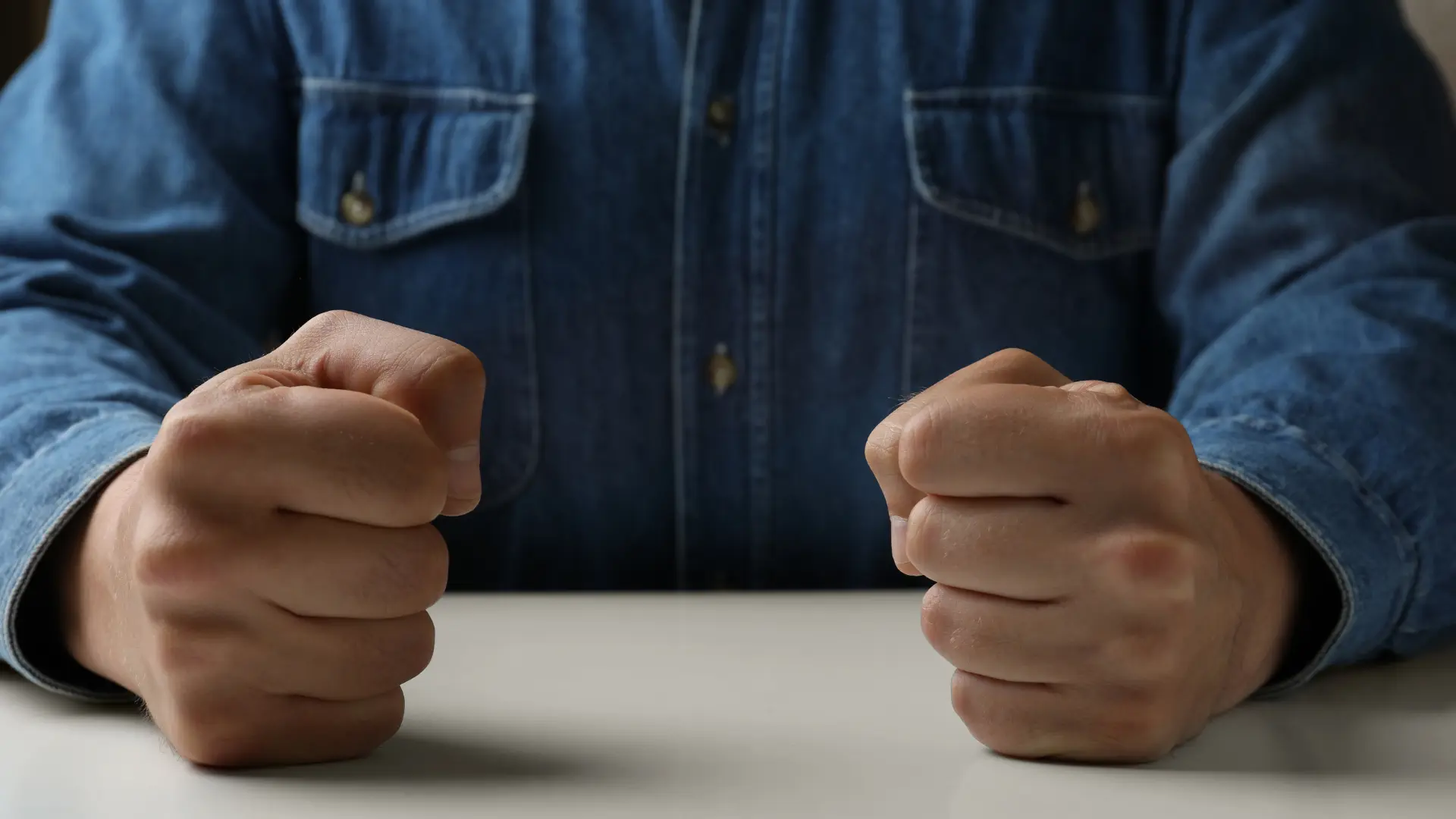 Person with clenched fists resting on table