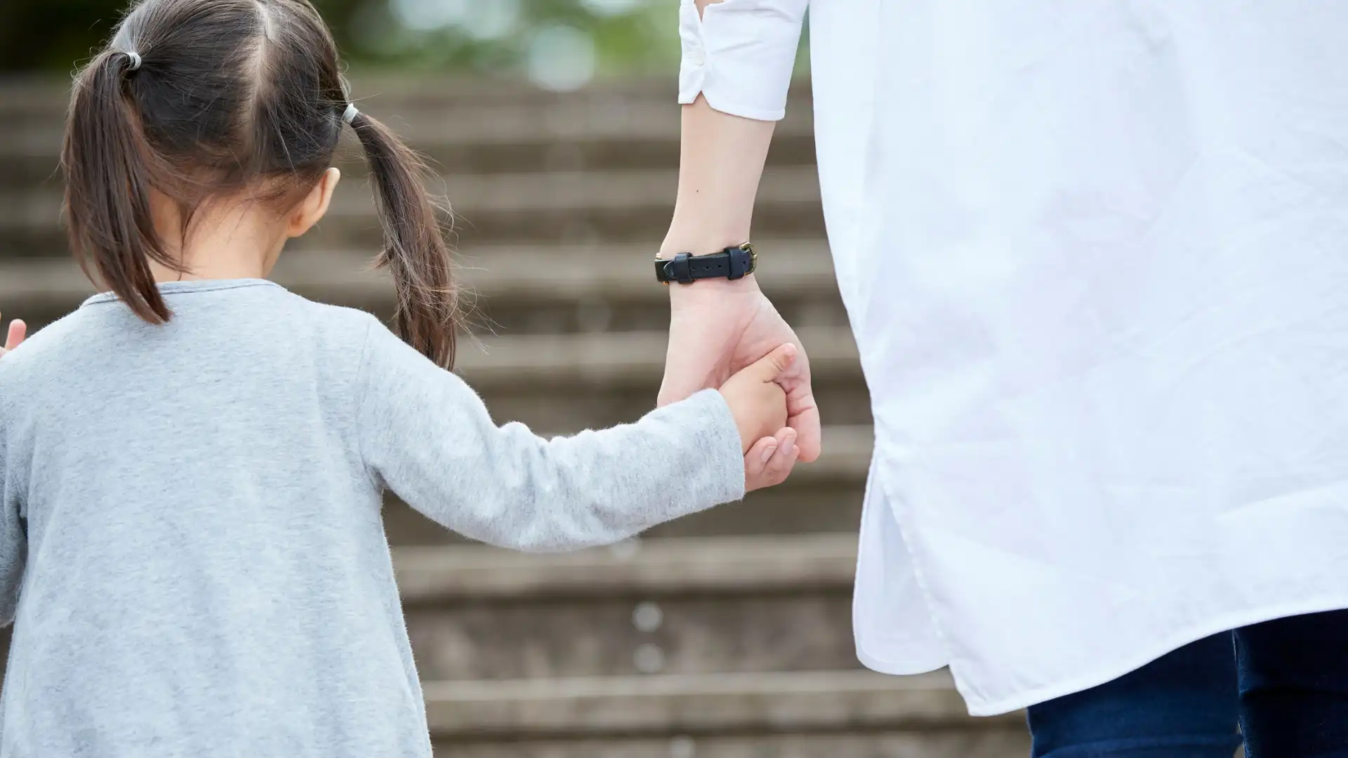 Adult holding young girl’s hand while walking up steps