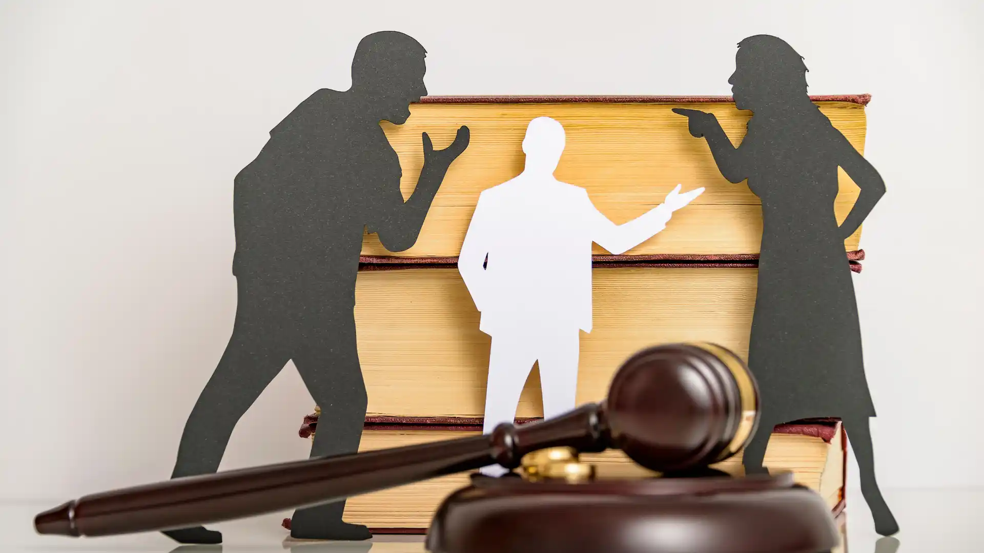 Paper cutouts of people arguing in front of law books with a gavel in the foreground.