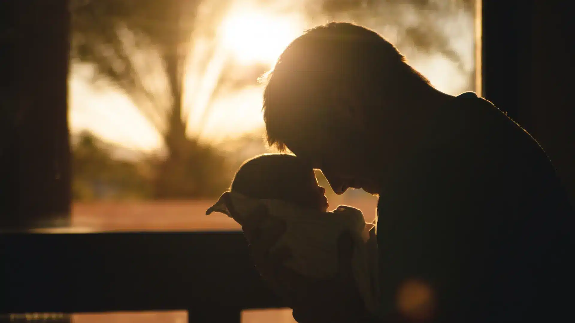 Person holding a child tenderly, silhouette at sunset.
