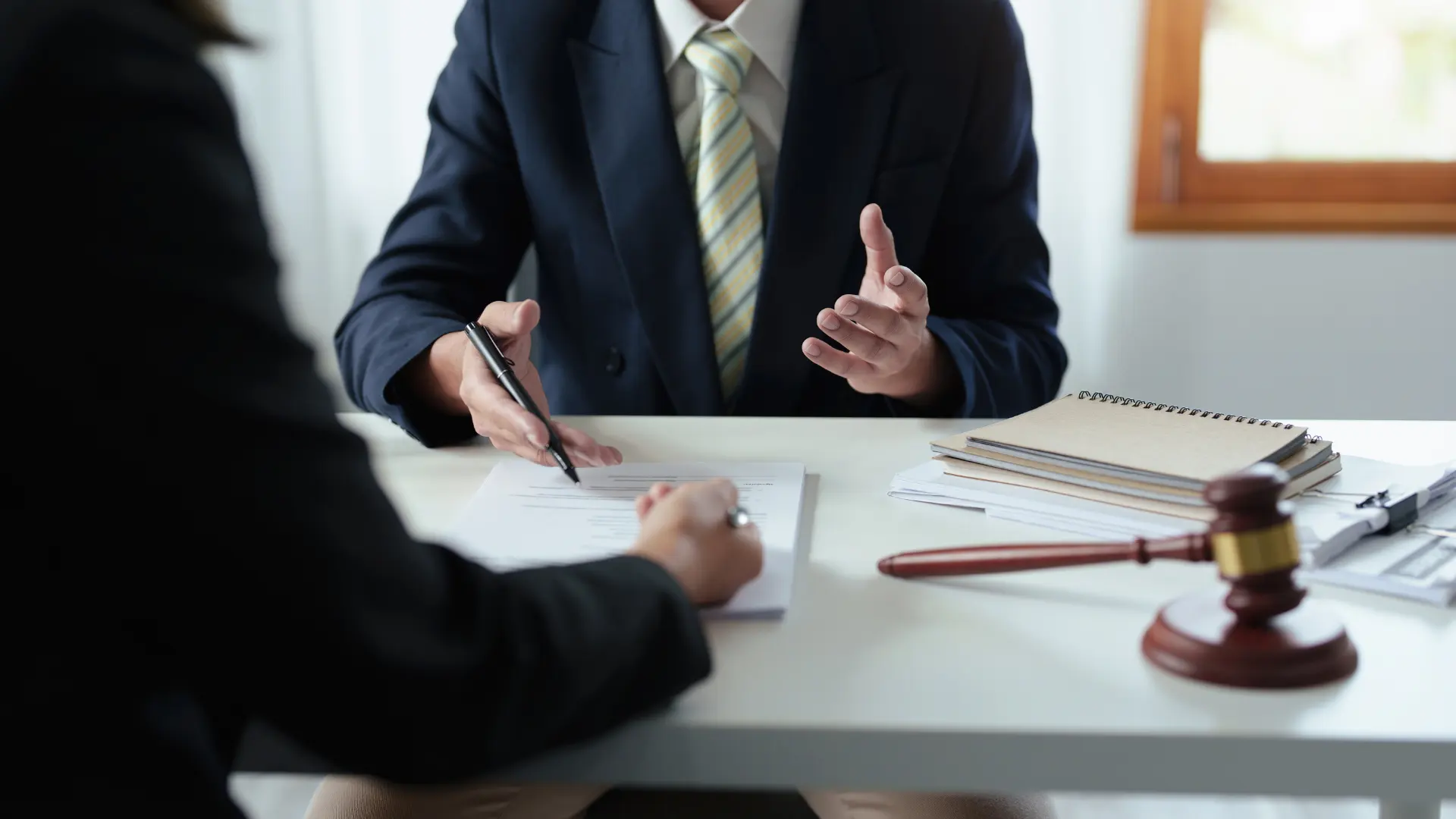 Businessperson in a suit discussing paperwork with a client across a desk.