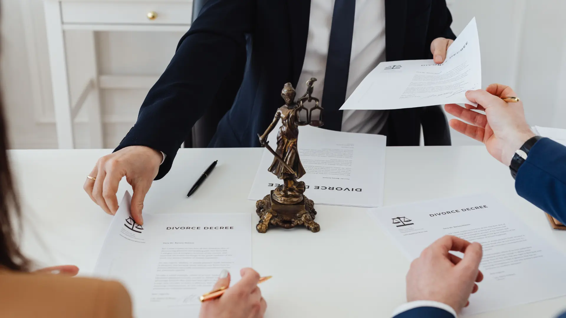 Lawyer handing documents across a table with a Lady Justice statue in the center.