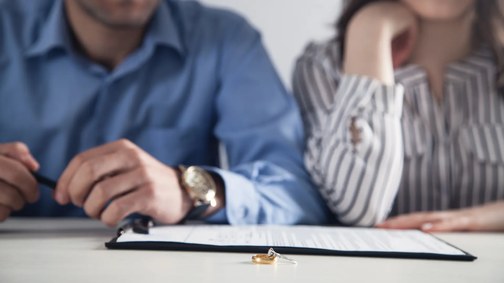 Couple sitting apart at a table with wedding rings placed on a document in front of them.